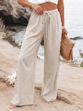 Beige linen drawstring wide leg pants with decorative pom-poms along side seams for stylish comfort