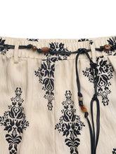 Beige boho print wide leg pants with black floral embroidery and a drawstring waist featuring wooden beads