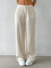 Beige linen wide-leg pants with front pockets and button closure featuring a relaxed wide leg design