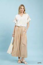 A woman wears umgee wide leg pants in tan and cream vertical stripes paired with a white blouse with lace sleeves
