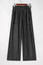 Black wide-leg trousers with elastic waistband, two front pockets, and smocked high waist for comfortable fit