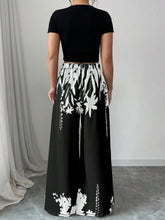 Black wide leg pants with bold white botanical print featuring stylized flowers and vines in maxi skirt style