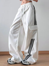White striped wide leg cargo pants featuring black three stripe side accents and a clear plastic thigh pocket