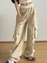 Beige cargo wide leg pants with a white elastic waistband and decorative bow tie details along the sides
