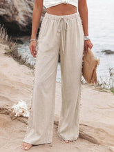 Beige linen wide leg pants with a drawstring waist and decorative pom pom trim along the side seams