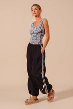A woman wearing a gray and white floral crop top paired with loose fit jogger pants with double lined side detail