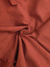 A soft rust-colored scarf with a textured weave and frayed edges complements frayed edge harem pants style
