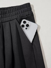 Black tied elastic high waist pleated sweatpants with side pocket holding a white smartphone