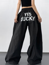 Back view of black letter back wide leg drawstring pants with yes lucky printed in bold white lettering