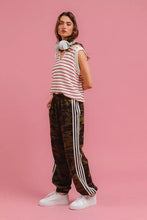 A woman wearing BiBi camouflage track pants in black with white side stripes paired with a white and red striped top