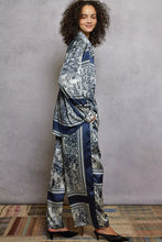 A flowing two-piece satin pajama set featuring a blue and white floral printed woven wide leg pant with navy stripes