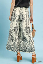 Cream-colored umgee border print wide-leg pants with intricate black botanical and paisley design and high-waisted elastic waistband