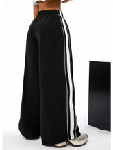 Black wide leg striped pants featuring bold white vertical stripes down the sides in track pant style