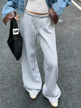 Light gray wide leg drawstring sweatpants with loose fit and brown leather pocket accents featuring care instructions