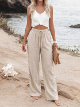 Beige linen drawstring wide leg pants with pom-pom trim along side seams and a comfortable drawstring waist