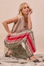 Woman wearing beige knit sleeveless top and bi bi leopard print pants with red side contrast and welt pockets