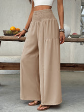 Beige smocked waist wide leg pants featuring a high-waisted design and soft flowing fabric