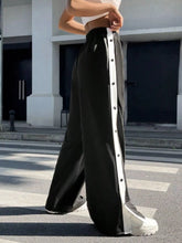 Black snap wide leg pants featuring white vertical stripe and button detailing along the side seam