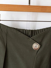 Olive green wide-leg button-accent pants with wrap-style design and decorative silver-toned embossed button detail