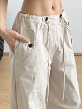 Beige relaxed wide-leg drawstring pants with black buttoned pockets and subtle stitching details for casual wear