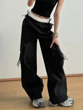 Black cargo pants with bow elastic waist, white elastic waistband, drawstrings, multiple pockets, and frayed detailing