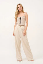 Beige crochet top with black lace-up front and thin straps paired with high-rise wide leg linen blended pants