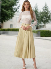 A woman wears high waist cream cropped pants with an a-line pleated skirt and lace top in soft beige tone