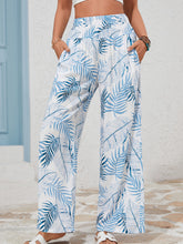 White wide-leg pants with a vibrant blue tropical print and shirred waistband in lightweight fabric for summer wear