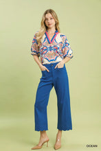 A woman wearing a vibrant patterned blouse stands in umgee scallop hem wide leg pants featuring a pink blue and white design