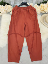 Rust-colored frayed edge harem pants with textured trim along sides and lower legs offering a stylish casual look