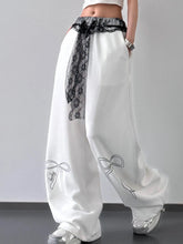 White satin wide leg pants with black lace belt trim and embroidered bow details on each leg