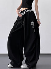 Black wide leg pants featuring a white drawstring lace waistband and embroidered rose detail on the side