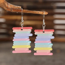 Acrylic rainbow dangle earrings shaped like striped spools