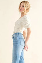 A cream-colored buttery soft ruched detailed jersey bodysuit with short sleeves and a fitted textured fabric
