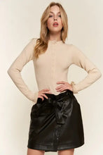 Black faux leather mini skirt with front bow paired with a round neck half button long sleeve bodysuit