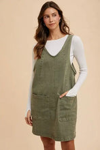 Olive green annie wear adjustable strap denim overall dress with front pockets worn over white long sleeve top