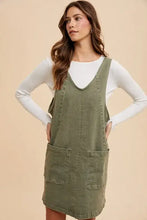 Olive green annie wear denim overall dress with adjustable straps, v-neckline, and front pockets over white top