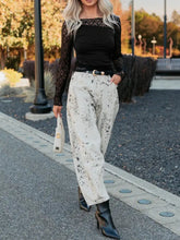 White pants with black splatter pattern paired with a high-waisted sheer floral lace long sleeve top with asymmetric panels