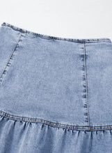 Light-wash denim mini skirt with tiered hem and visible stitching featuring an asymmetric ruffle overlay design