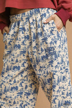 Cream-colored umgee scenic print casual sweatpants featuring a blue winter scene with trees cabins and skiers