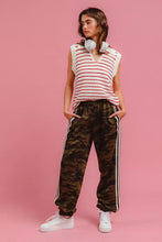 A woman wearing a white and red striped knit sleeveless top paired with BiBi camouflage track pants