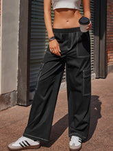 Black wide leg pants with white contrast stitching and multiple pockets in a cargo style design