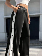 Black two-tone snap wide leg pants with white vertical stripe and black snap buttons down the side seam