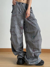 Gray plaid wide leg pants with a drawstring waist and bold graffiti style print featuring stars and reversed text