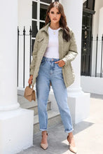 Olive green khaki quilted jacket with high collar, white top, light blue jeans, beige heels, tan purse