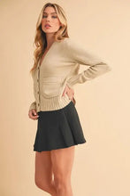 Cream cardigan with ribbed hem button closure, knit pockets, and black pleated skirt