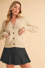 Beige cardigan with ribbed hem button closure, ruffled sleeves and black pleated skirt