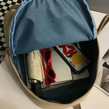 Beige cotton backpack bag with blue lining holding red sunglasses, notepad, colorful phone case
