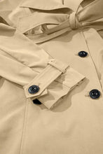 Beige double-breasted trench coat with black buttons and white belt