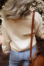Cream sweater with ruffled sleeves, light blue jeans, and brown leather crossbody bag